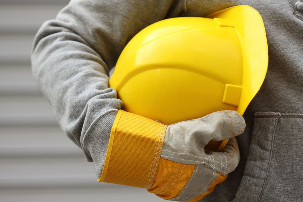 a construction worker wearing grey, holding their yellow hardhat